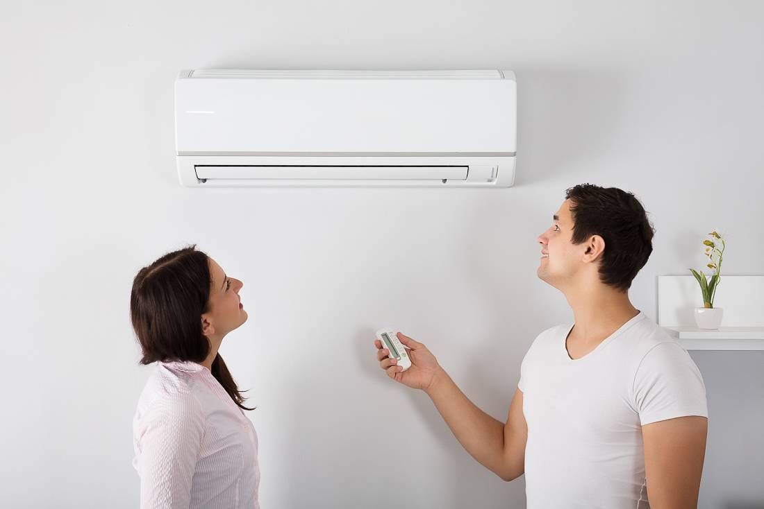 Two people controlling a wall-mounted air conditioner with a remote